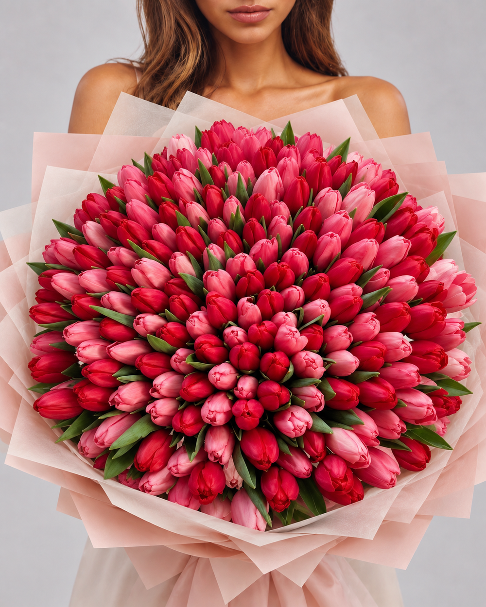 Bouquet Yara de tulipes rouges et roses fraîches porté par une femme, papier rose pâle